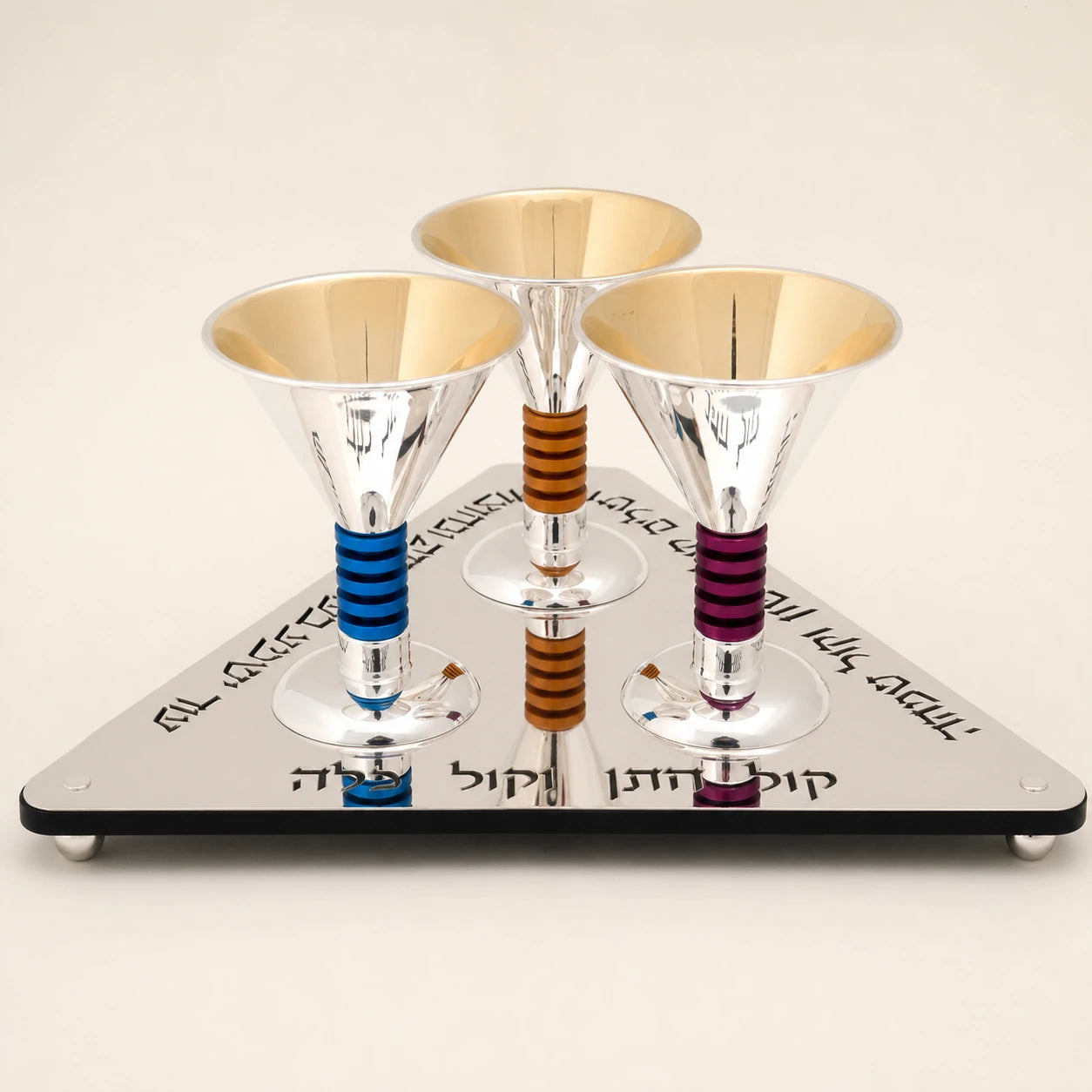 Three silver ceremonial cups with blue, amber, and purple grips on a sculptural triangular base